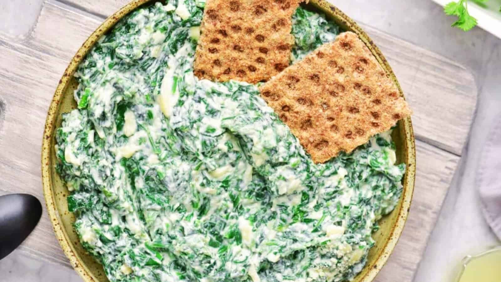 A bowl of creamy spinach dip with two crispbread crackers on top, capturing the nostalgic charm of retro appetizers.
