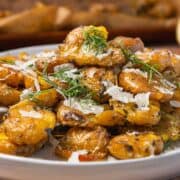 Crispy smashed potatoes topped with fresh dill and grated cheese on a white plate.