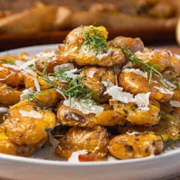 Crispy smashed potatoes topped with fresh dill and grated cheese on a white plate.