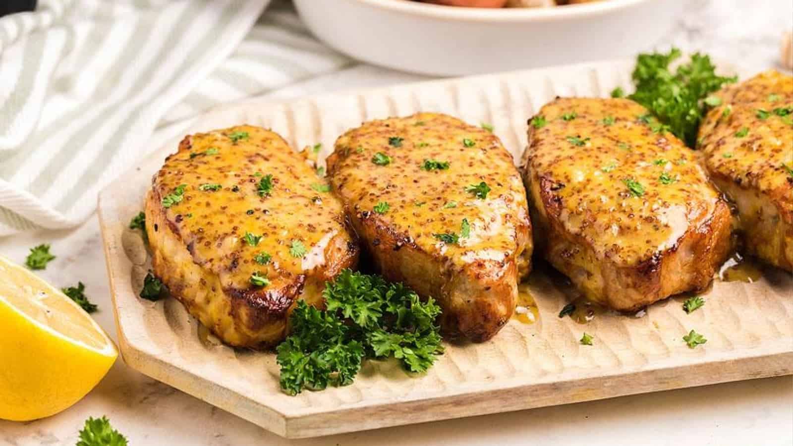 Four glazed pork chops garnished with parsley on a platter, with a lemon half on the side.