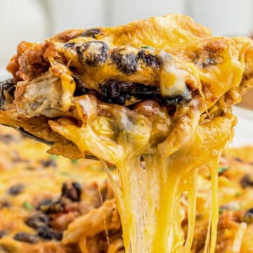 A cheesy, baked casserole with beans and melted cheese being lifted with a spoon.