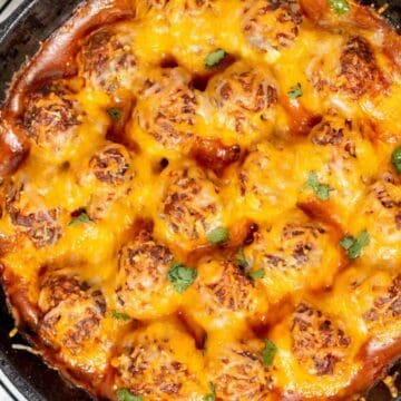 Cheesy baked meatballs in tomato sauce, topped with melted cheese and cilantro, perfect for celebrating Cinco de Mayo in a cast iron skillet.