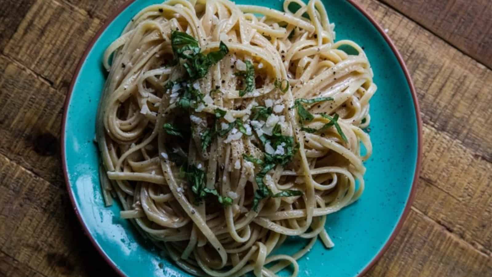A plate of spaghetti with grated cheese, cracked pepper, and fresh herbs on a turquoise dish&mdash;one of those easy budget side dishes perfect for any meal.