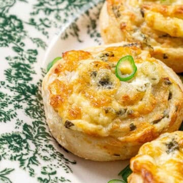 Golden, cheesy puff pastry pinwheels with herbs on a decorative green and white plate.
