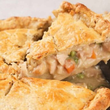 A slice of homemade chicken pot pie with vegetables is being lifted from a pie pan.