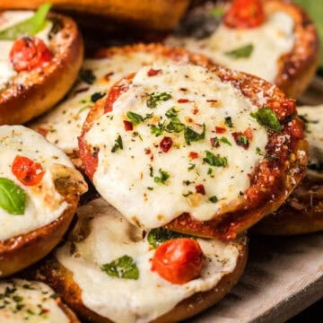 Mini bagels topped with melted cheese, tomato, and herbs arranged on a wooden board.