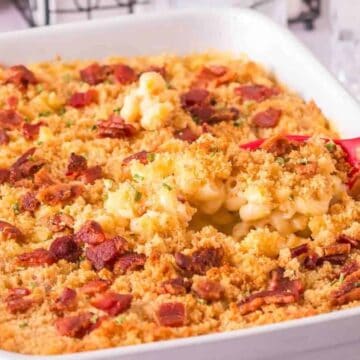 Baked macaroni and cheese topped with crispy breadcrumbs and bacon pieces in a white casserole dish.