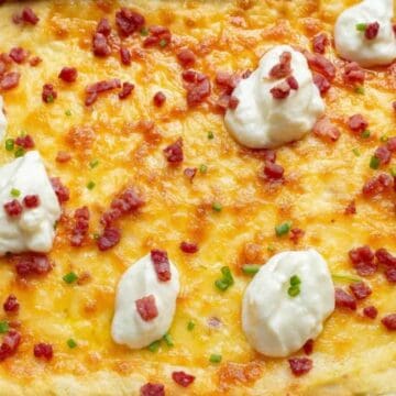 Cheesy baked casserole topped with dollops of sour cream, chopped bacon, and green onions in a red dish—one of the best easy budget side dishes for any meal.