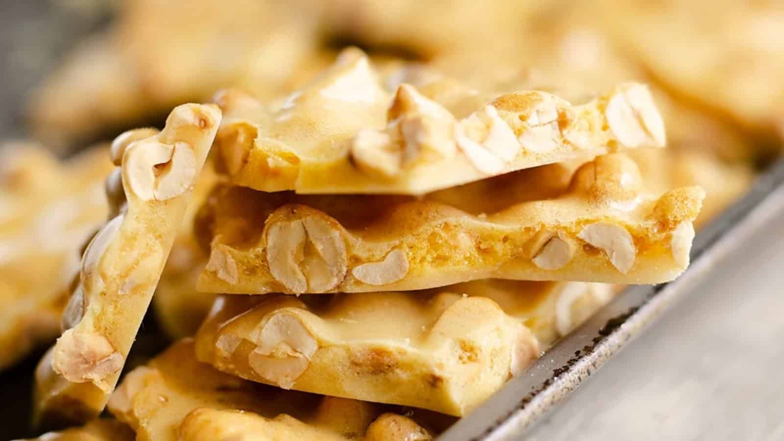 Close-up of stacked pieces of peanut brittle with visible peanuts and a golden, glossy, crunchy texture.