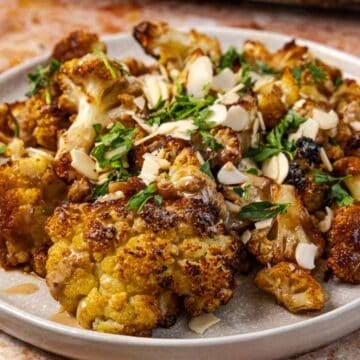 Middle Eastern Roasted Cauliflower topped with fresh herbs, sliced almonds, and a drizzle of sauce on a plate.