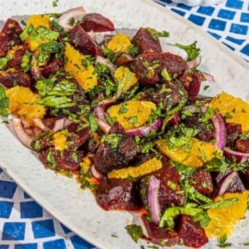 A plate of beet salad with orange slices, red onion, and fresh herbs on a white dish.
