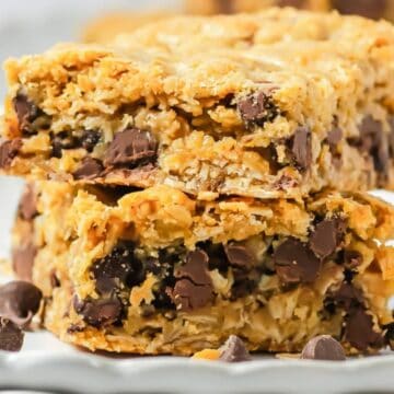 Two stacked oatmeal chocolate chip bars on a white plate with chocolate chips scattered nearby.