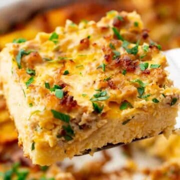 A spatula lifts a cheesy, baked casserole slice topped with herbs and browned bits.