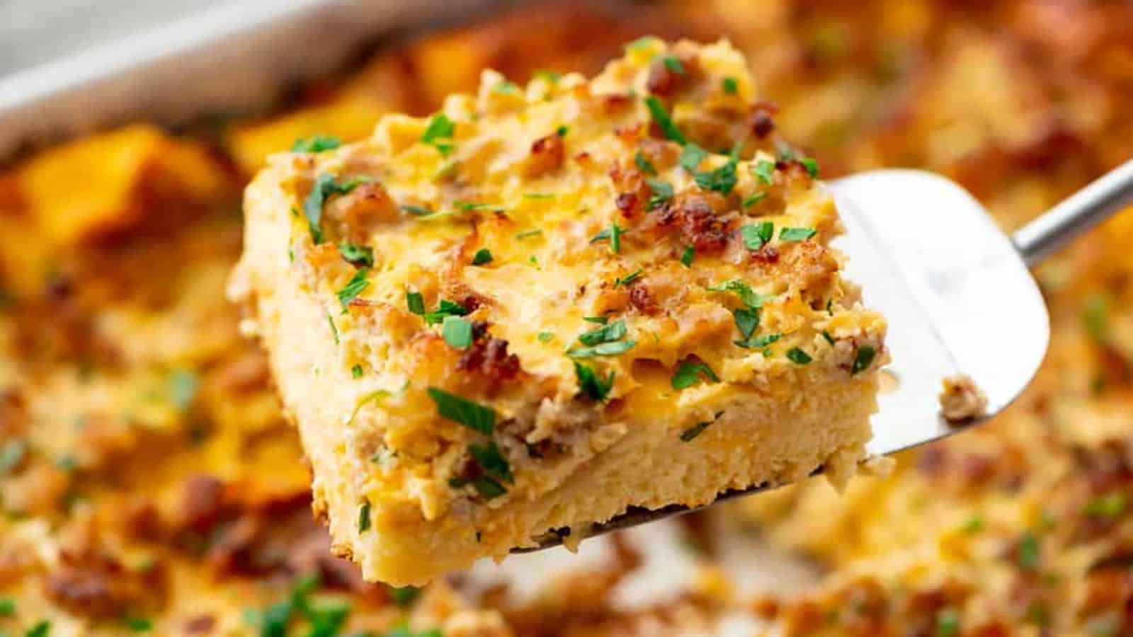 A spatula lifts a cheesy, baked casserole slice topped with herbs and browned bits.