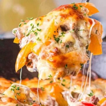A cheesy, baked casserole with yellow peppers and herbs is being lifted from a skillet with melted cheese stretching.