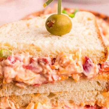 A stacked sandwich filled with creamy pimento cheese, topped with a green olive on a toothpick.