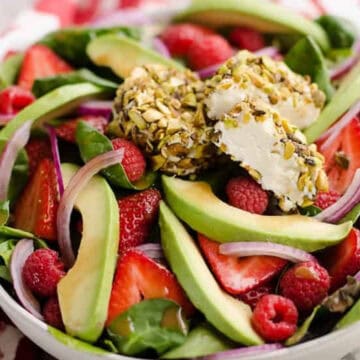 Salad with spinach, strawberries, raspberries, avocado, red onion, and cheese coated in chopped nuts.