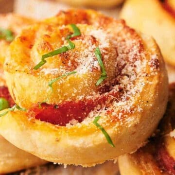 Close-up of a pizza roll topped with grated cheese and fresh basil on a plate with other rolls.