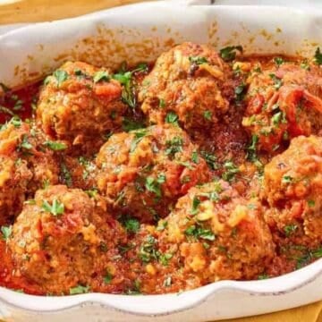Baked meatballs in tomato sauce, garnished with chopped herbs in a white dish on a yellow cloth.