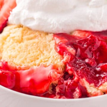 Strawberry cobbler topped with whipped cream in a white bowl, garnished with a fresh strawberry slice.