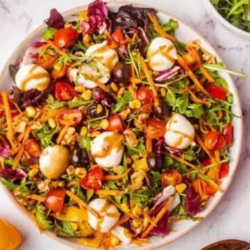 Colorful salad with greens, cherry tomatoes, carrots, olives, corn, and dressing on a white plate, shot from above.