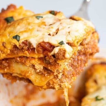 A close-up of a cheesy, baked lasagna slice being lifted from a pan.