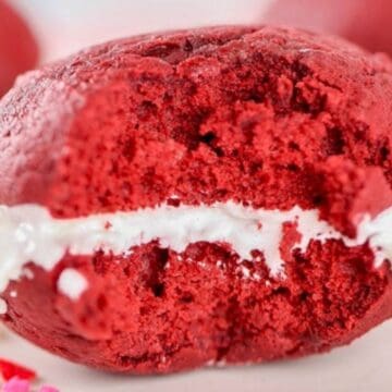 A red velvet whoopie pie with white cream filling and a bitae taken out of it.