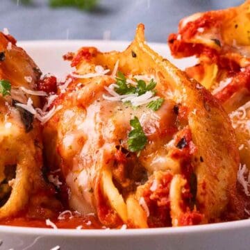 Stuffed pasta shells topped with melted cheese, marinara sauce, and parsley on a white plate.