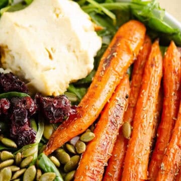 Salad bowl with roasted carrots, mashed potatoes, dried cranberries, pepitas, and fresh greens.
