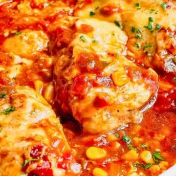 Baked chicken breasts in a tomato-based sauce with corn and herbs, served in a white dish.
