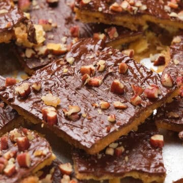 Squares of chocolate toffee topped with chopped nuts, arranged on a baking sheet.