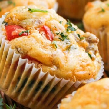 Close-up of savory muffins with herbs, tomato pieces, and cheese in white paper liners.