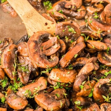 Sautéed mushrooms with herbs in a pan, stirred with a wooden spoon.