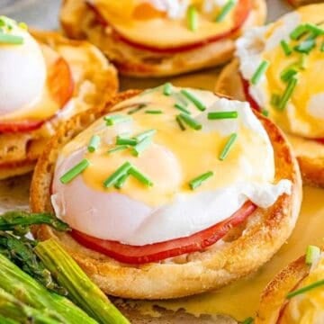 Eggs Benedict on toasted English muffins with ham, topped with hollandaise sauce and chives, served with asparagus.