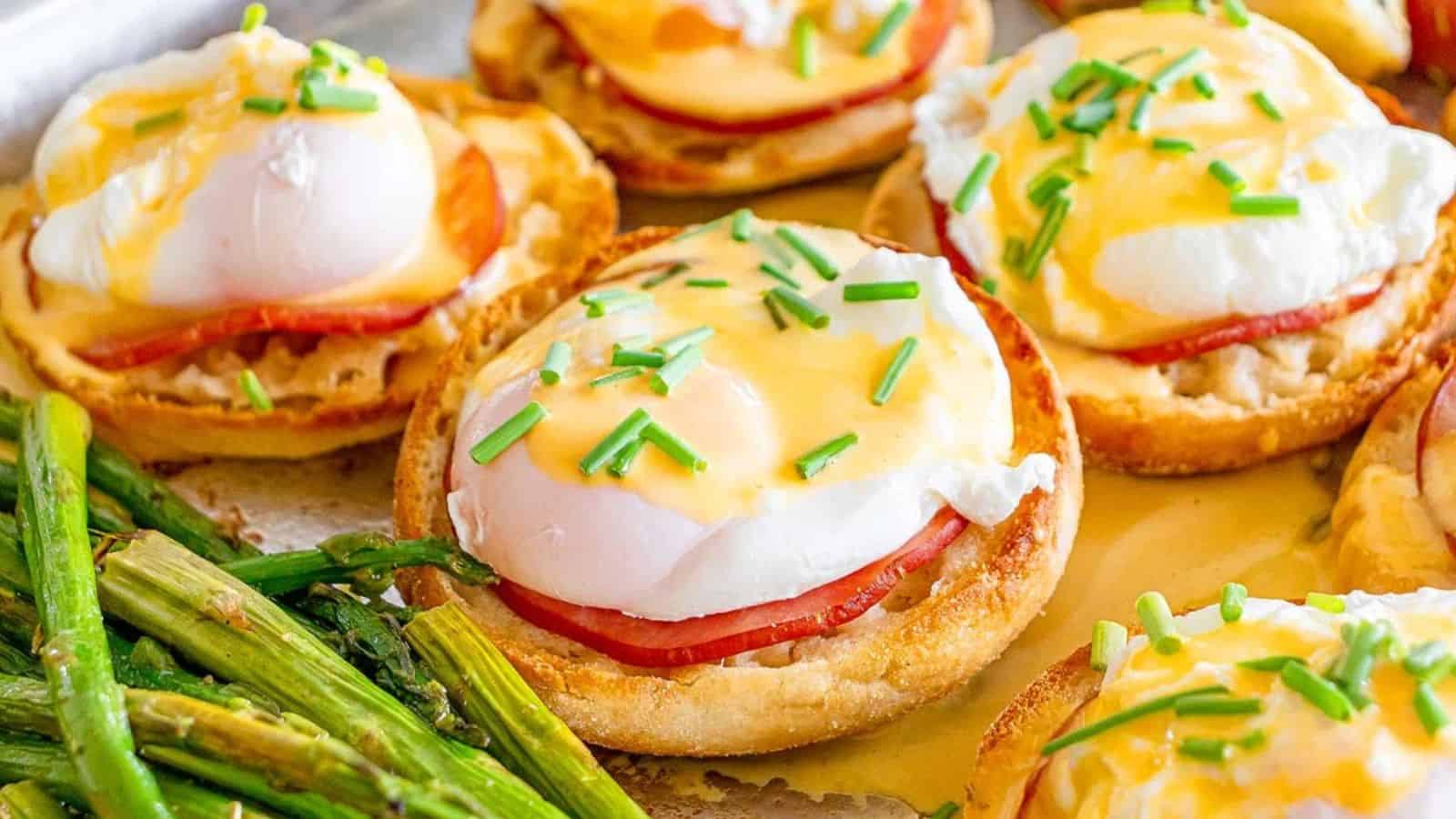Eggs Benedict on toasted English muffins with ham, topped with hollandaise sauce and chives, served with asparagus.