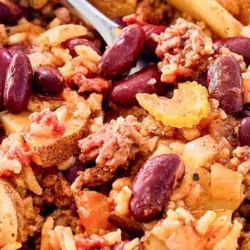A close-up of a hearty casserole with ground beef, kidney beans, rice, potatoes, and tomatoes in a white bowl.