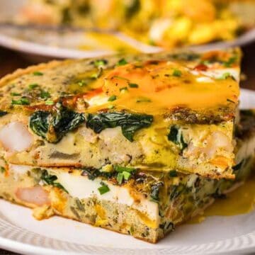 Two slices of vegetable and herb frittata with runny yolk on a white plate.
