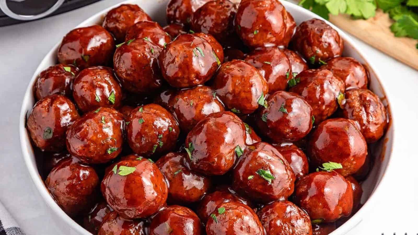 A bowl filled with glazed meatballs garnished with chopped parsley&mdash;perfect as easy graduation party appetizers.