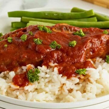 White rice topped with a tomato-based sauce and herbs, served with green beans on a white plate.