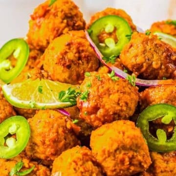 Spicy meatballs garnished with lime slices, jalapeño rings, and red onion on a white plate.