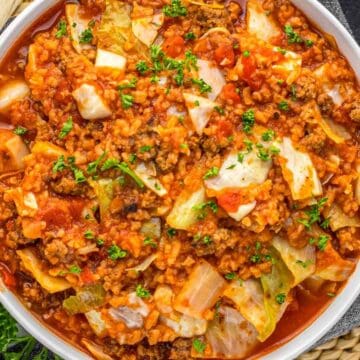 A bowl of cabbage roll soup with ground meat, tomatoes, and herbs, garnished with fresh parsley.