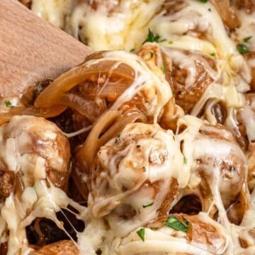 Meatballs with melted cheese, caramelized onions, and herbs, being served with a wooden spoon—perfect for those who love easy Crockpot Meals.