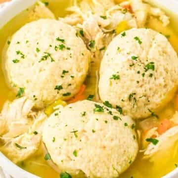Bowl of chicken and dumplings soup with shredded chicken, vegetables, and three large dumplings, garnished with herbs.