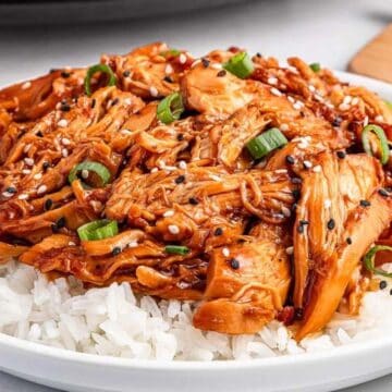 Shredded teriyaki chicken garnished with sesame seeds and green onions served over white rice on a plate.