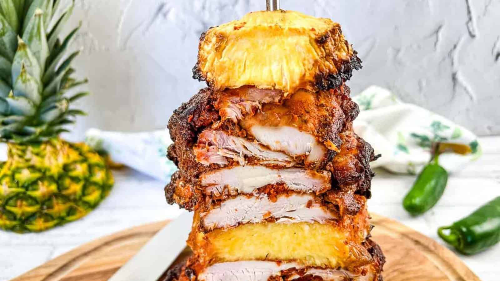 A stack of chicken and pineapple on a vertical skewer on a cutting board.