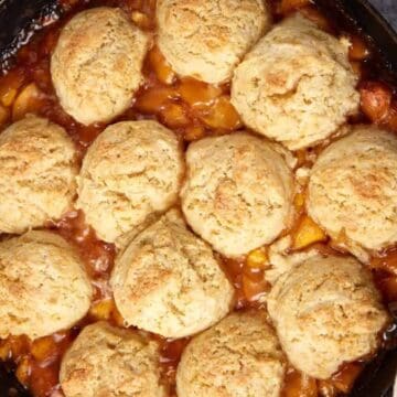 A cast iron skillet filled with peach cobbler topped with golden, fluffy biscuits—a nod to vintage recipes and timeless comfort.