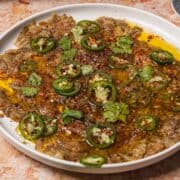 A plate of Spicy Eggplant Carpaccio dip topped with sliced jalapeños, cilantro, olive oil, and chili flakes.
