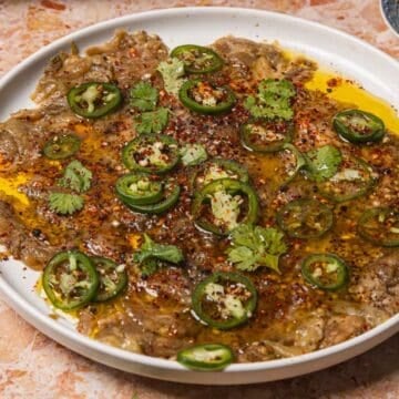 A plate of Spicy Eggplant Carpaccio dip topped with sliced jalapeños, cilantro, olive oil, and chili flakes.