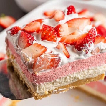 A layered strawberry dessert with whipped cream and fresh strawberries on top, served on a spatula.