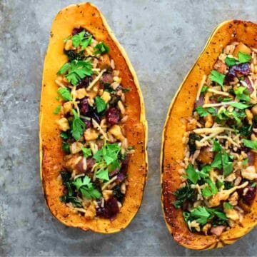 Two stuffed roasted squash halves filled with veggies and herbs, garnished with fresh parsley on a rustic surface.